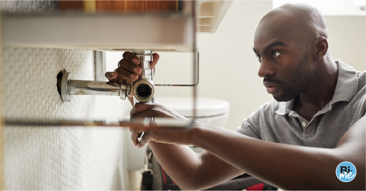 A man working on pipes below a sink